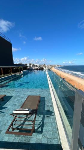 a swimming pool with a bench and the beach at Apartamento charmoso com Rooftop in Salvador