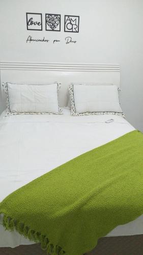 a white bed with a green blanket on it at Apartamento Kobrasol - Ótima localização in São José