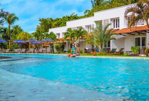 a man sitting on the edge of a swimming pool in front of a resort at Hotel Pipa Atlântico in Pipa