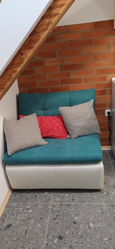a green couch with two pillows on a brick wall at HIŠA MARGIT, Studio APARTMA in Rateče