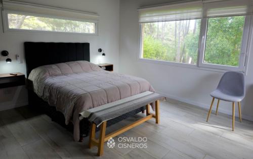 ein Schlafzimmer mit einem Bett, einem Stuhl und zwei Fenstern in der Unterkunft Los Patitos in Mar de las Pampas