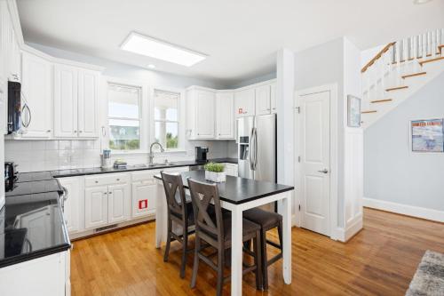 a kitchen with white cabinets and a black table and chairs at Oceanfront w Pool Panoramic Deck Views 5BDR Folly Ocean Breeze by AvantStay in Folly Beach