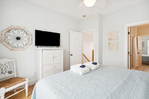 a white bedroom with a bed and a flat screen tv at Oceanfront w Pool Panoramic Deck Views 5BDR Folly Ocean Breeze by AvantStay in Folly Beach