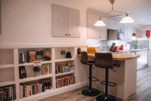 a kitchen with a bar with two chairs and bookshelves at Riverbank Cottage in Ironbridge