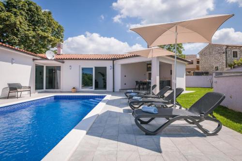 a pool with chairs and an umbrella next to a house at Ferienhaus Nana in Marčana