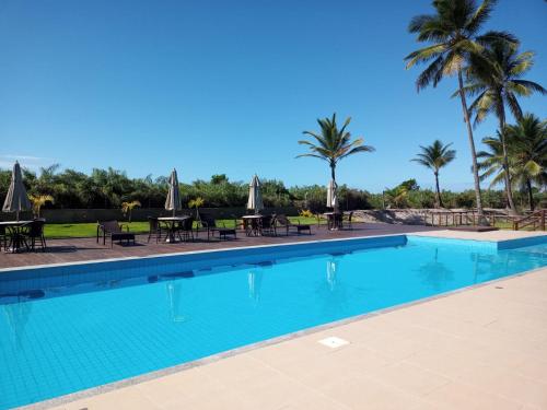 a swimming pool with tables and chairs and palm trees at Lindo apto em frente ao Mar - Ilhéus - Itacaré Ba in Ilhéus