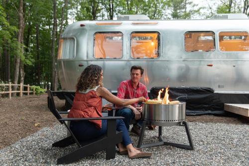 a man and woman sitting around a fire in front of a trailer at AutoCamp Sequoia in Three Rivers