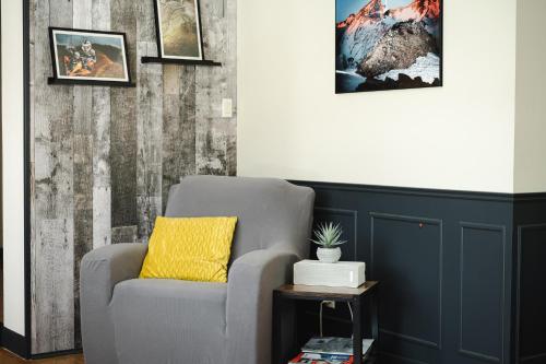 a gray chair with a yellow pillow in a room at La Maison du Sentier - Foyer et Mt Porphyre in Murdochville