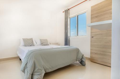 a white bedroom with a bed and a window at Precioso apartamento en Serena Village in Punta Cana