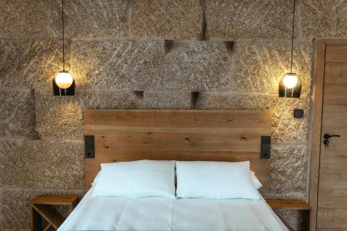 a bedroom with a stone wall with a bed and two lights at La Molinera Casa Rural - Ribeira Sacra in Campo