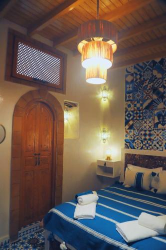 a bedroom with a blue bed and a chandelier at Dar Milal in Essaouira