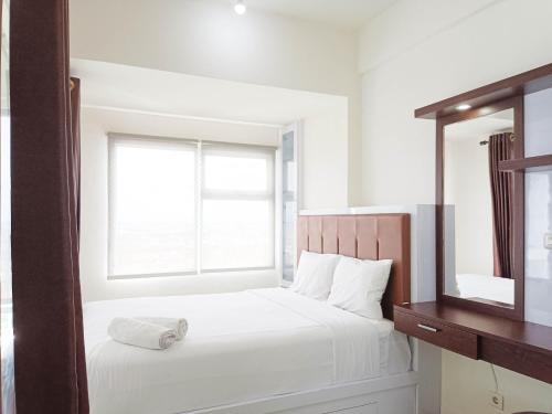 a white bedroom with a bed and a mirror at Comfort 1BR at Vida View Makassar Apartment By Travelio in Pampang