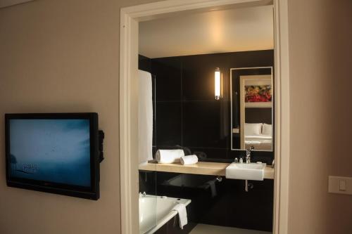 TV y baño con espejo y lavabo. en AXSUR Design Hotel en Montevideo