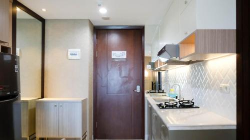 a kitchen with a wooden door and a kitchen counter at Nice and Relax 1BR at Grand Sungkono Lagoon Apartment By Travelio in Surabaya