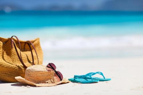 a straw hat and a pair of blue flip flops and a beach bag at Royale Suites by Arc Royal Luxury Apts in Anse Royale
