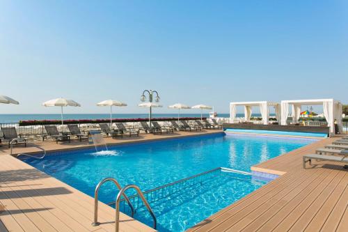 a swimming pool with chairs and umbrellas next to the ocean at Victoria Frontemare Beach & Spa Hotel Jesolo in Lido di Jesolo