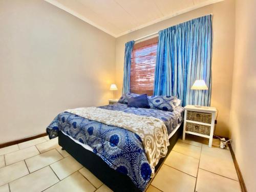 a bedroom with a bed and a window with blue curtains at Seaside Haven in Pearly Beach