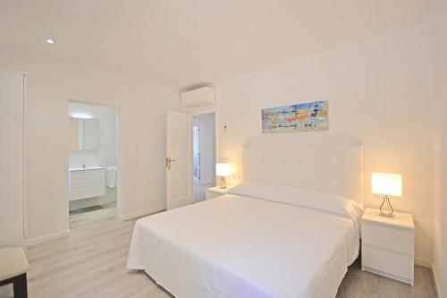a white bedroom with a white bed and two lamps at House PINOCHA in Can Picafort