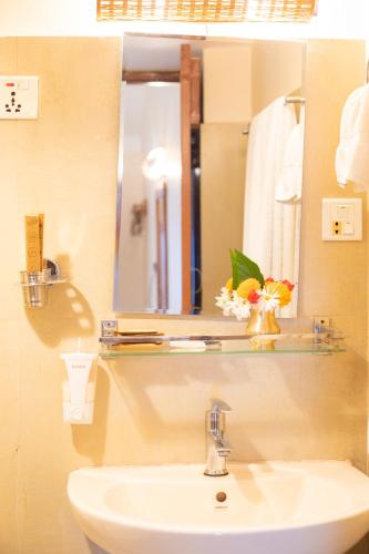 a bathroom sink with a mirror and a vase of flowers at Prakriti Resort and Organic Farm Pvt. Ltd. in Burhānilkantha