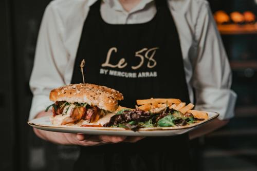 a person holding a plate with a sandwich and french fries at Mercure Arras Centre Gare in Arras