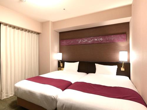 a hotel room with two beds and a window at Smile Hotel Premium Kanazawa Higashiguchiekimae in Kanazawa