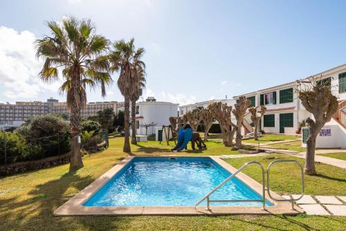 a pool in a yard with palm trees and a building at Menorca Apartamento ALOHA by Mauter Villas in Cala en Blanes