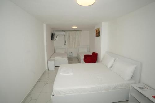 a white bedroom with a white bed and a red chair at Enles Hotel in Durrës
