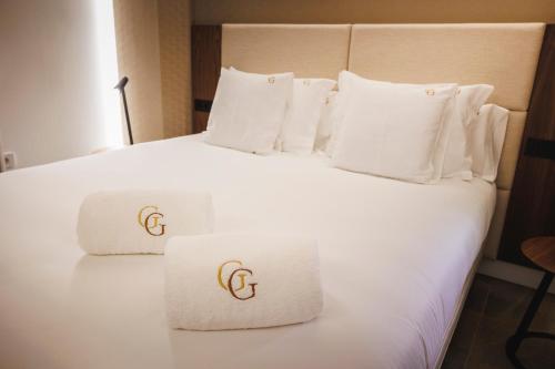 a white bed with white pillows and gold logos on them at Corral del Carbón GG Luxury Hotel Boutique in Granada