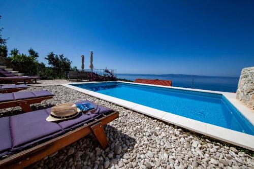 a swimming pool with a table and chairs and the ocean at Wunderschöne Steinvilla Mit Tollem Ausblick in Podgora