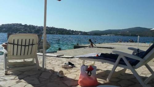 ein Strand mit zwei Stühlen und Menschen im Wasser in der Unterkunft Ferienhaus mit Terrasse und Kinderpool an einer Bucht mit Meerblick in Rogoznica