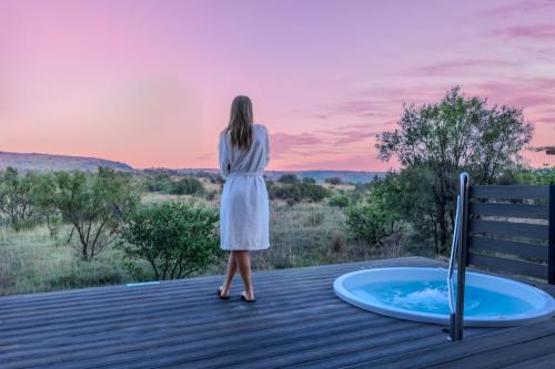 a woman in a white dress standing on a deck next to a hot tub at Cradle Boutique Hotel in Lanseria