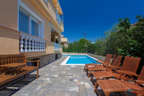 a swimming pool with wooden chairs next to a house at Gästezimmer Tina 6 in Šilo