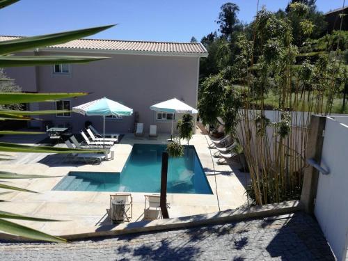 a swimming pool with chairs and umbrellas next to a house at Casa dos Barros - Vitorino dos Piães in Vitorino dos Piães