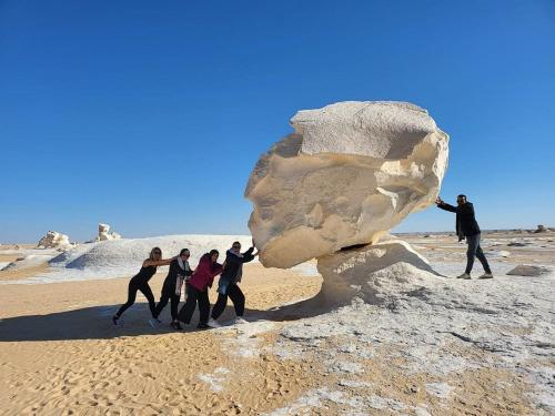 a group of people standing around a rock in the desert at White Desert Safari With Camping in Bawiti