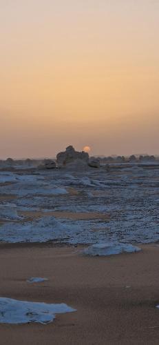 a sunset on the beach with the sun setting in the background at White Desert Safari With Camping in Bawiti