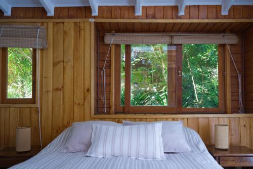a bed in a wooden room with two windows at Cabañas El Albaricoque Cochiguaz in El Sanjeado