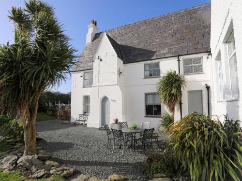 a white house with a table and chairs and palm trees at School House in Aberffraw
