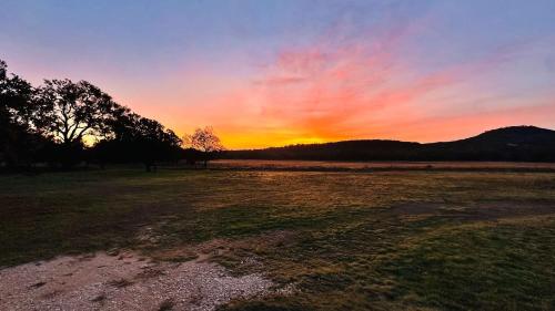 an open field with a sunset in the background at Kingsby Farmhouse - 1BR with 2 Queens & Mountain Views in Boerne
