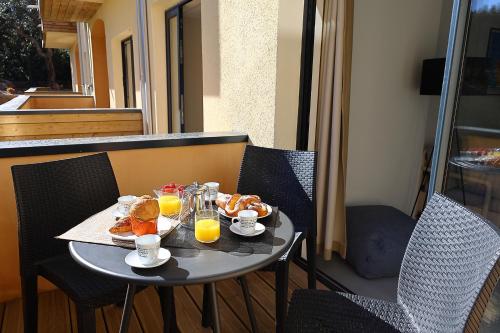 - une table avec des aliments pour le petit-déjeuner et du jus d'orange sur un balcon dans l'établissement Casa di Daisy - T2 les pieds dans l'eau et piscine, à Pianottoli-Caldarello