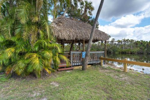 a hut with a palm tree and a fence at Riverside Hut Cozy Getaway w Tiki Hut & Grill in Bradenton