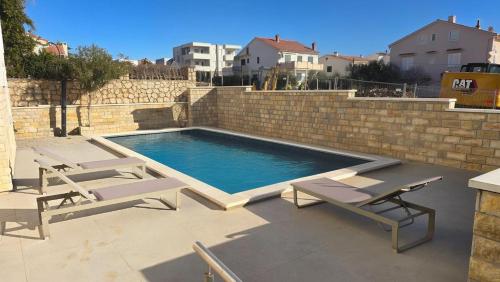 een zwembad met 2 ligstoelen naast een bakstenen muur bij CRYSTAL WAVE Apartments in Novalja