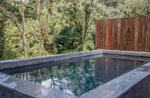 a swimming pool with a wooden fence and trees at Riverside Haven Elegant House with Serene Forest in San Simon El Alto