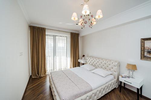 a white bedroom with a large bed and a chandelier at The Central Collection Apartments in Chişinău