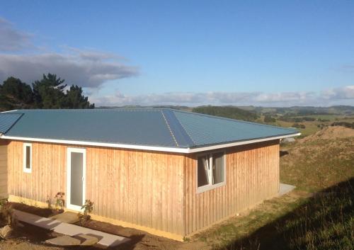 a house with a metal roof on top of a field at Pukeatua Farmstay in Waimauku