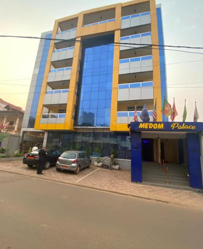 a yellow and blue building with cars parked in front of it at Résidence hôtelière MEDOM Palace, Bastos in Yaoundé