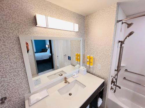 a bathroom with a sink and a mirror and a tub at Home2 Suites By Hilton Pensacola Airport Medical Center in Pensacola