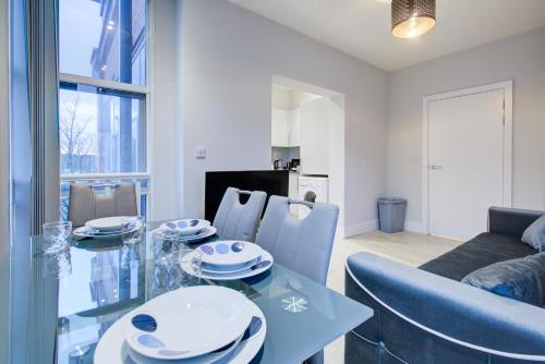 a dining room with a glass table and blue chairs at 1 BR Flat 6 Mins From Heathrow Airport Flat 18 in Harmondsworth