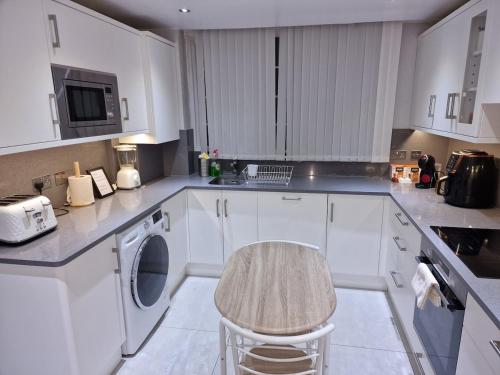 a white kitchen with a washing machine and a stool at NightRest Homes Smart TV In Each Room - Parking - Hemel Hempstead in Hemel Hempstead