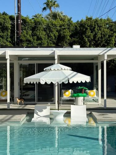a house with a swimming pool and an umbrella and chairs at Aerhaus - Mid-Century Oasis in Palm Springs