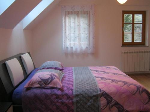 a bedroom with a bed with a purple comforter and a window at House Dolenja Trebuša in Dolenja Trebuša